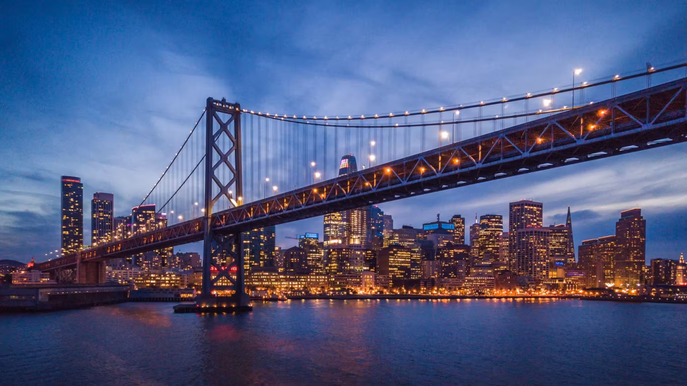 The Bay Bridge lit at dusk with the San Francisco skyline behind it