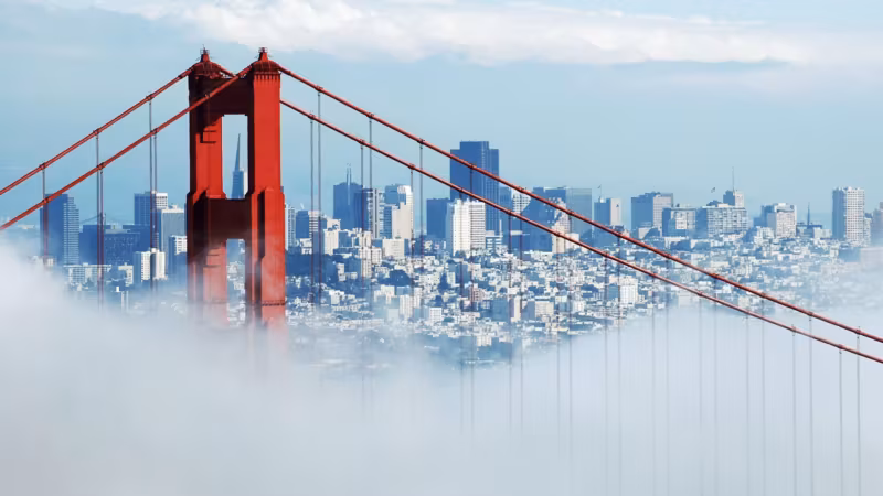 A Golden Gate Bridge tower rising above low fog with the city beyond