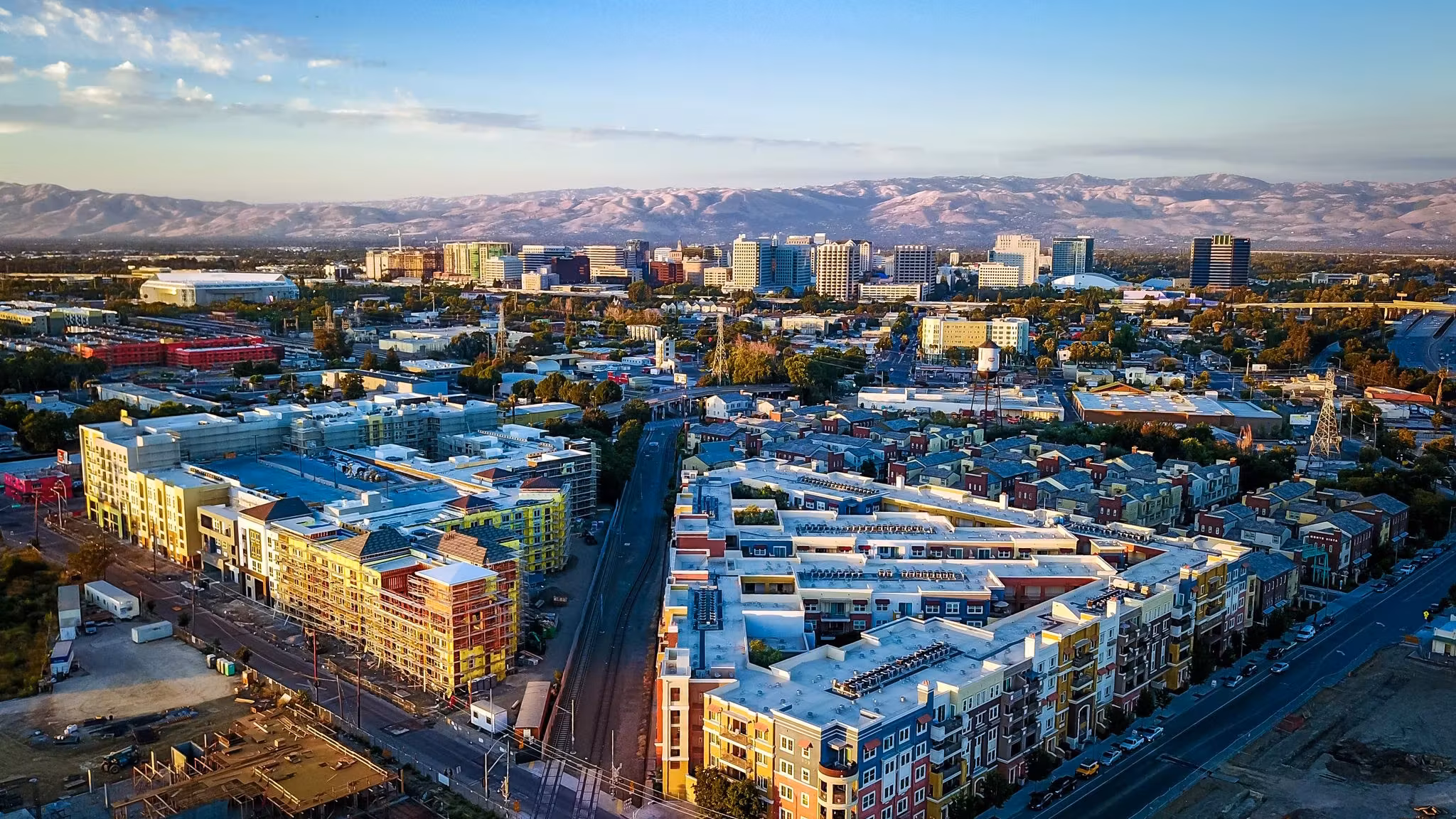 Aerial view of downtown San Jose with light-rail tracks running between low buildings and the hills beyond