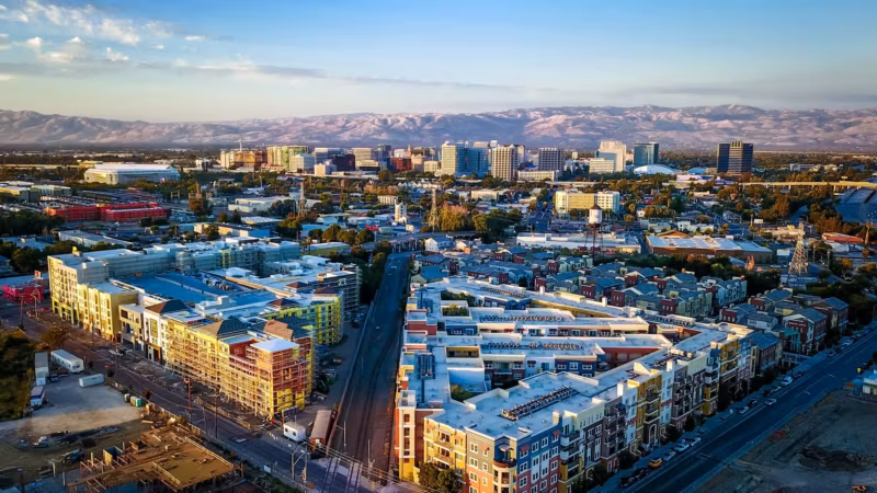 Aerial view of downtown San Jose with light-rail tracks running between low buildings and the hills beyond