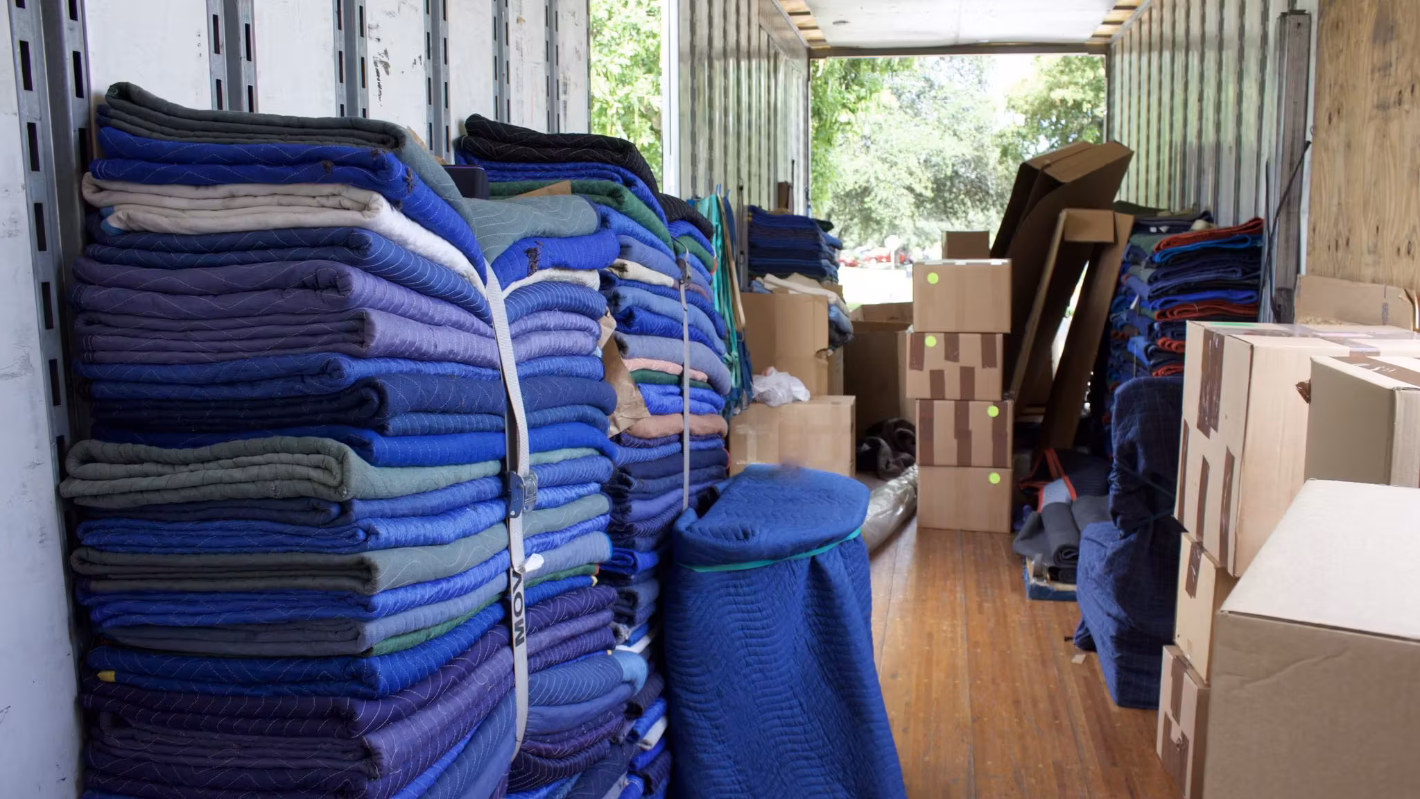Folded quilted moving blankets stacked inside a truck beside cartons