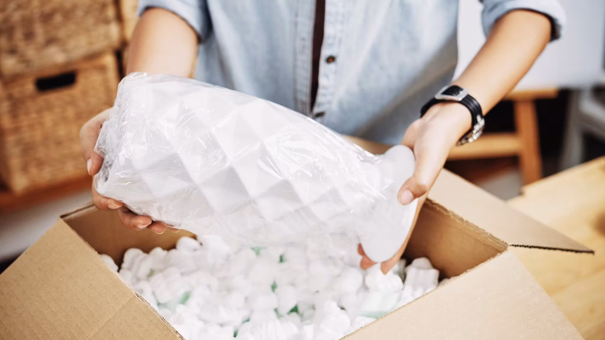 Hands lowering a bubble-wrapped object into a carton