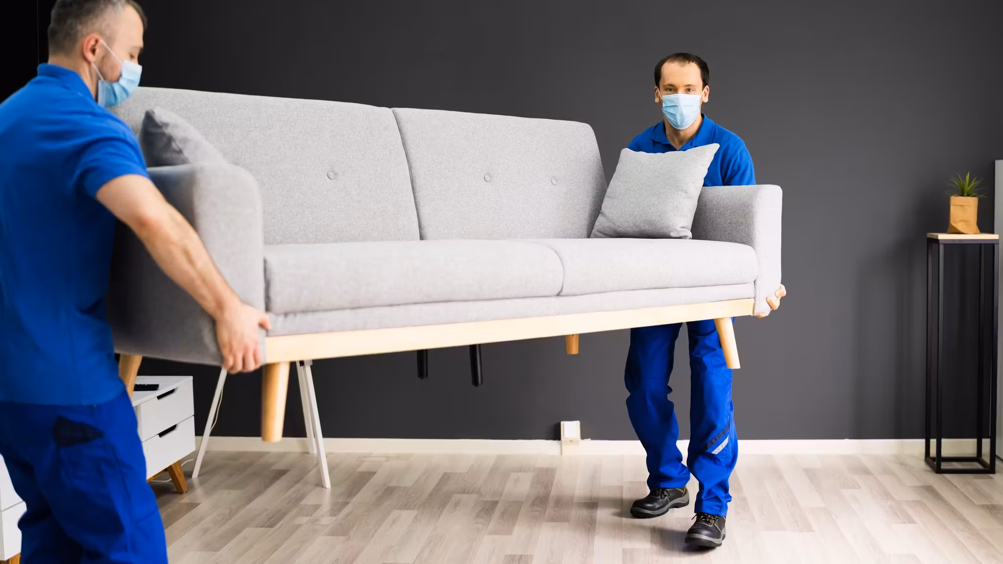 Two movers carrying a pale sofa through a room