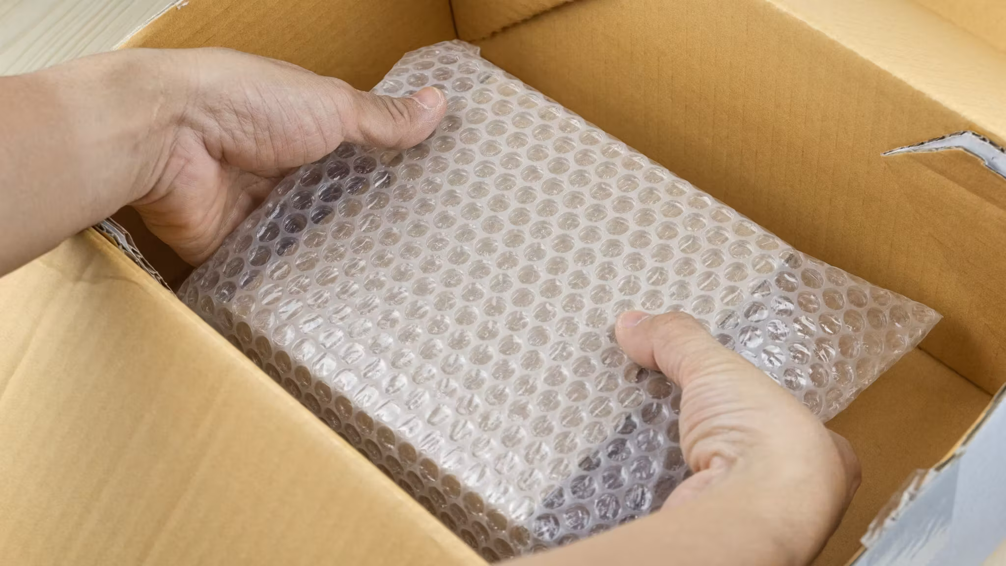 Hands laying a bubble-wrapped item into a lined carton