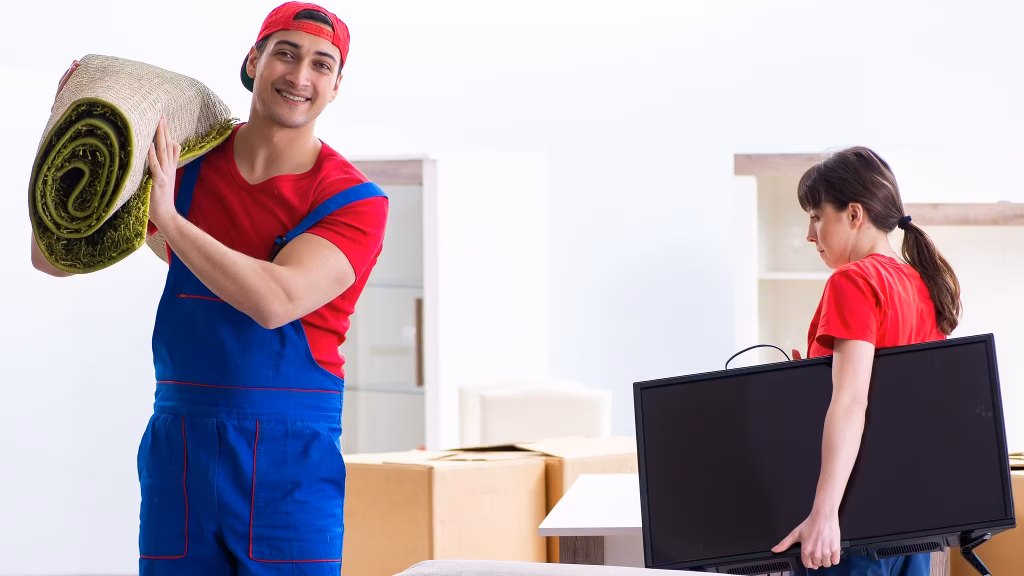 A mover with a rolled rug on his shoulder while a second carries a flat screen
