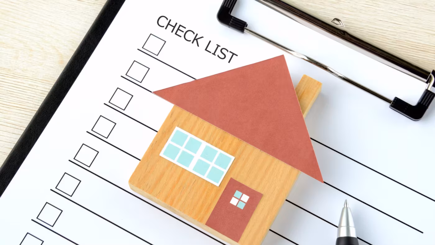 A printed checklist on a clipboard beside a paper house cut-out