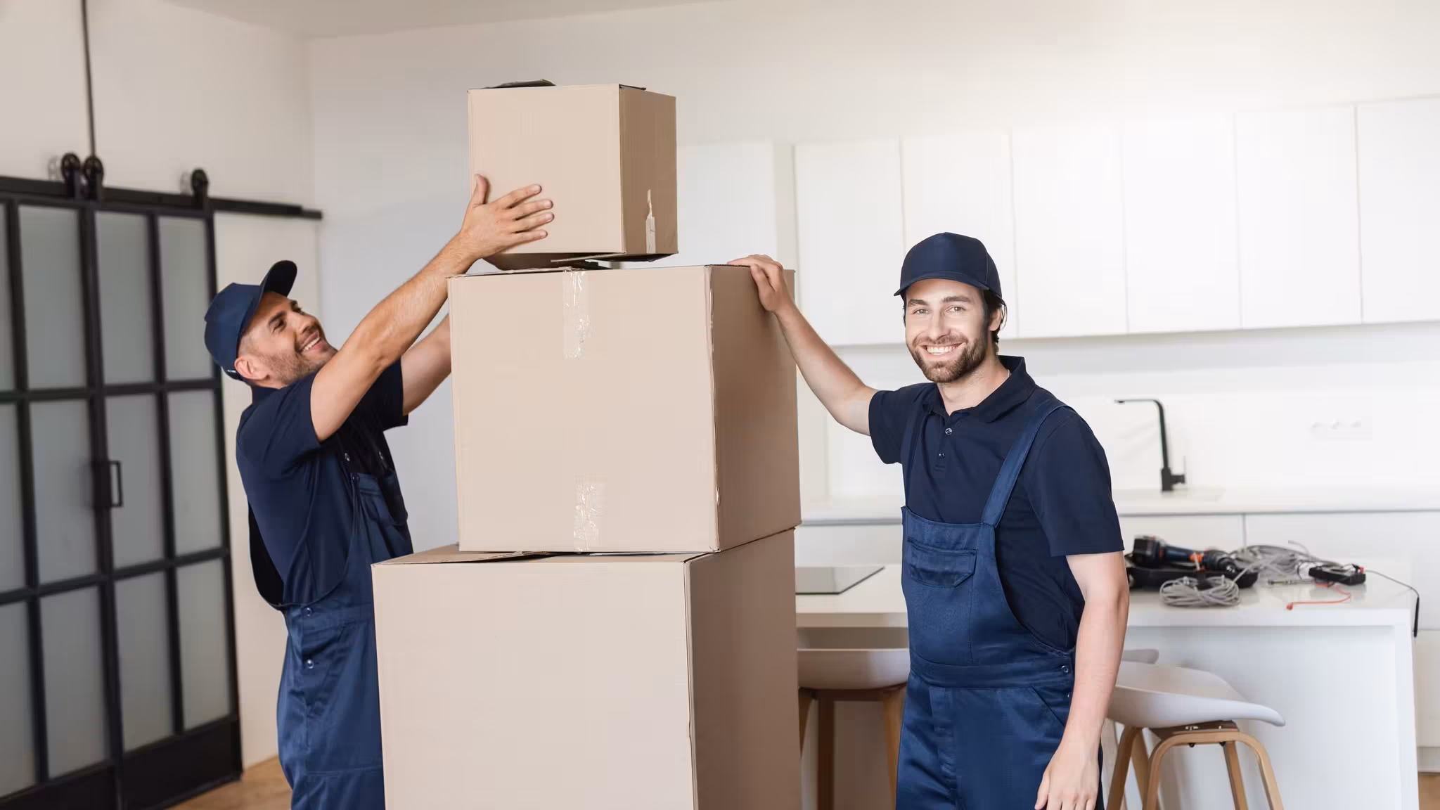 Two movers stacking cartons on a kitchen worktop, one steadying the pile