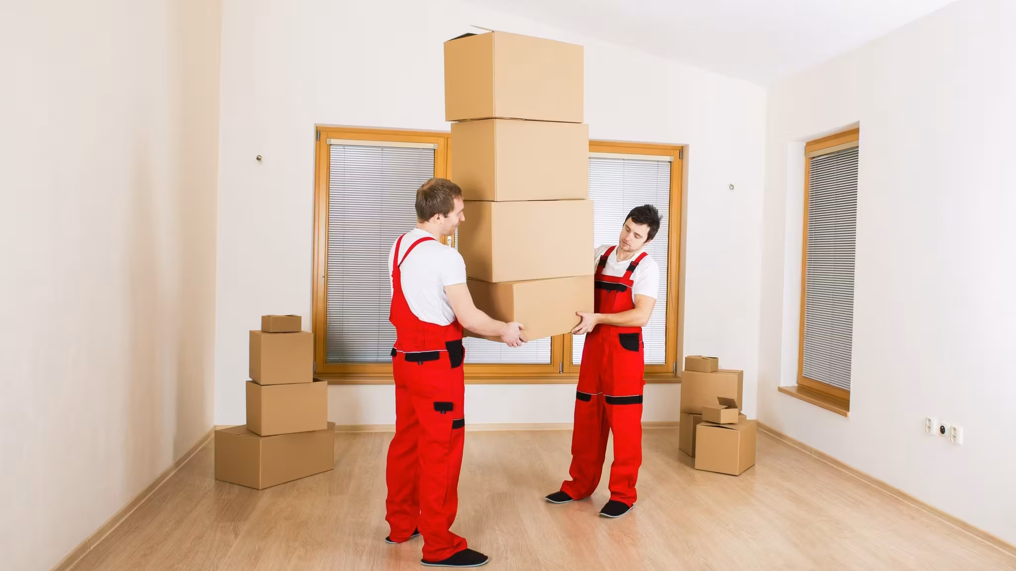 Two movers carrying a tall stack of cartons across an empty room