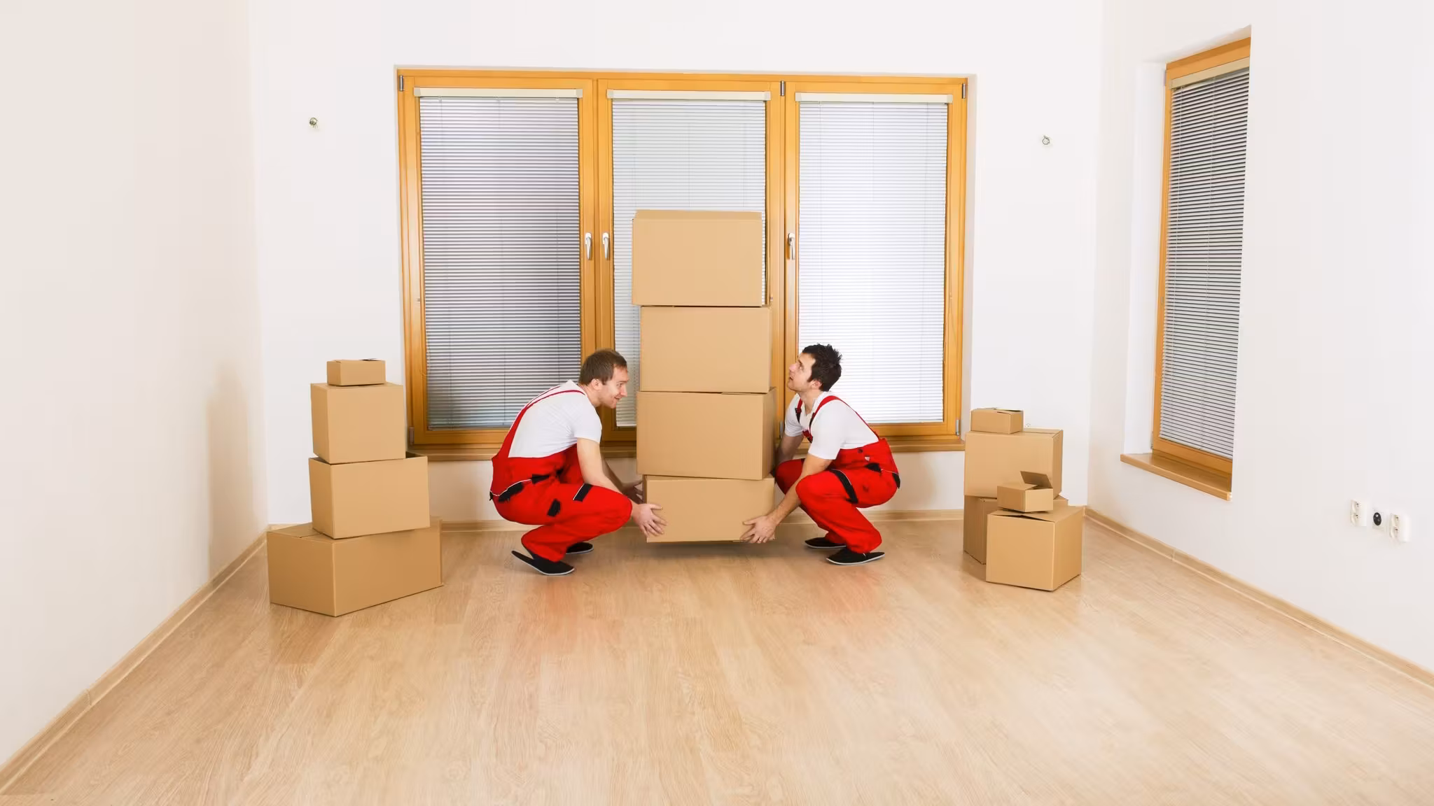 Two movers crouched over cartons by a window in an empty room