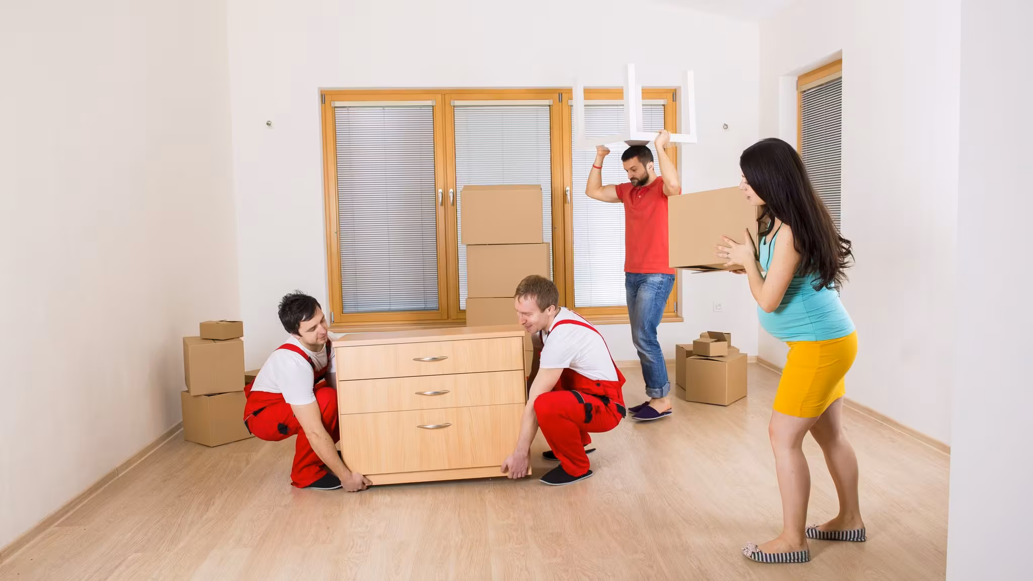 Two movers lowering a chest of drawers into place while a couple direct them