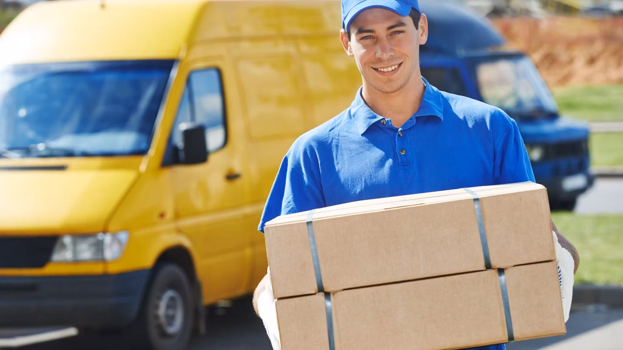 A mover holding a strapped carton beside a yellow van
