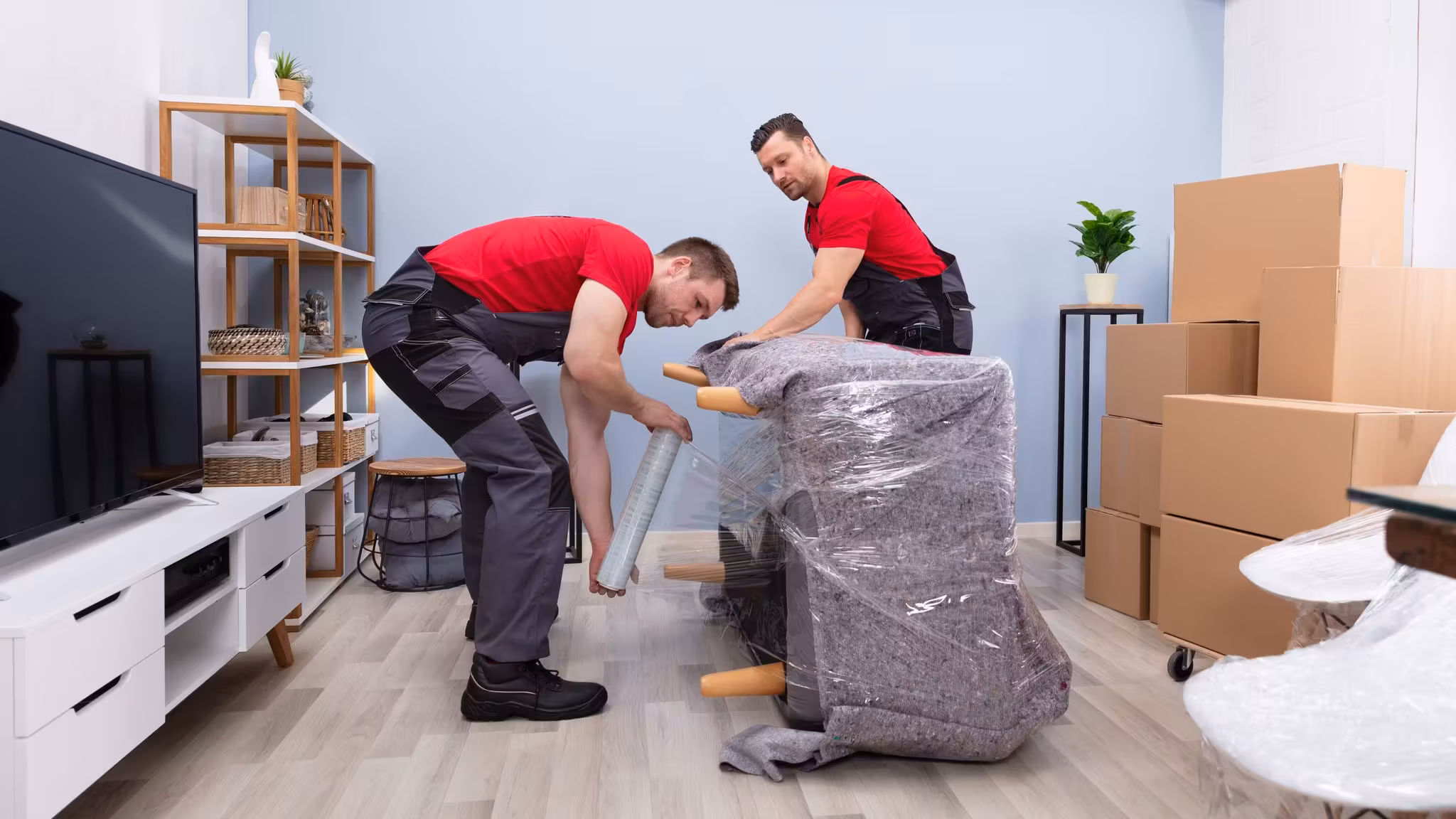 Two movers taking the wrapping off a chair in a living room stacked with cartons
