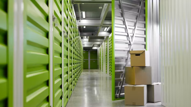 An aisle of green unit doors with a few cartons and a step ladder part-way down it
