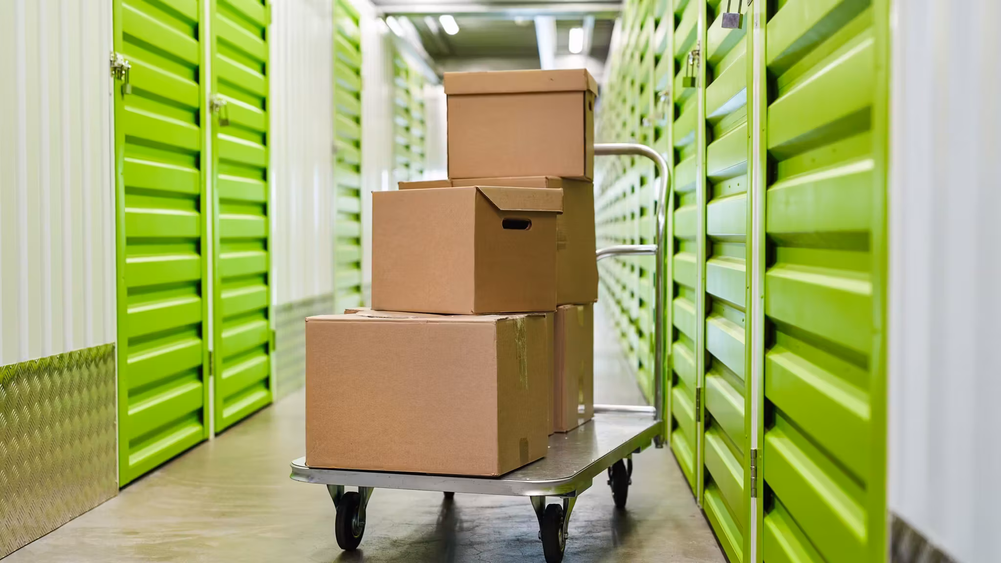 Cartons stacked on a flatbed trolley in an aisle between bright green unit doors