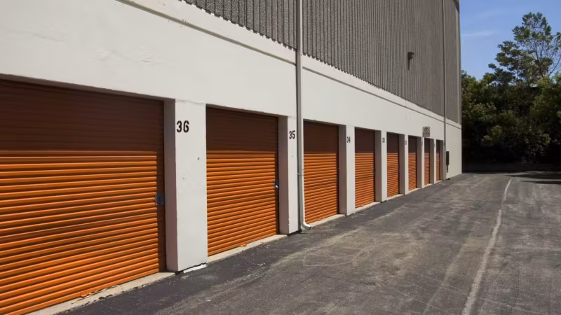 A row of orange roll-up doors along the outside of a single-storey storage building