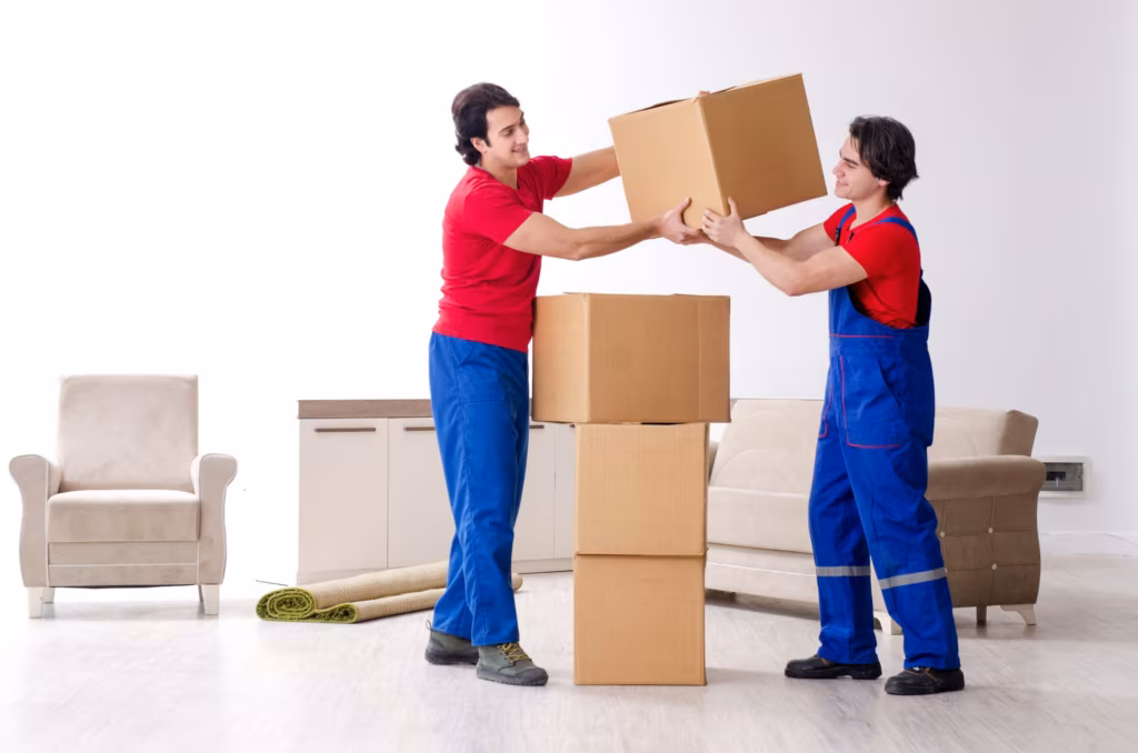 Two movers in bib overalls stacking cartons in a part-emptied living room