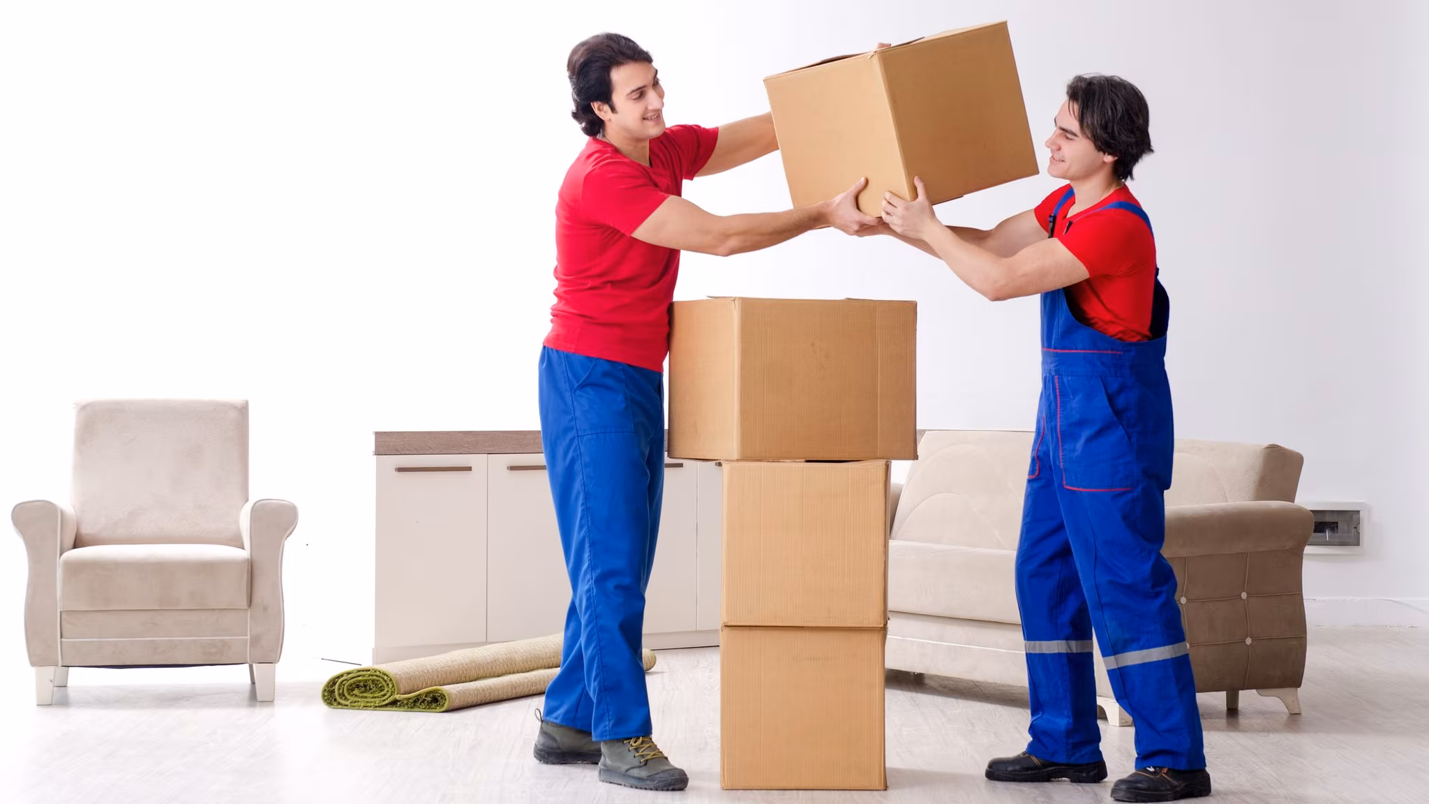 Two movers in bib overalls stacking cartons in a part-emptied living room