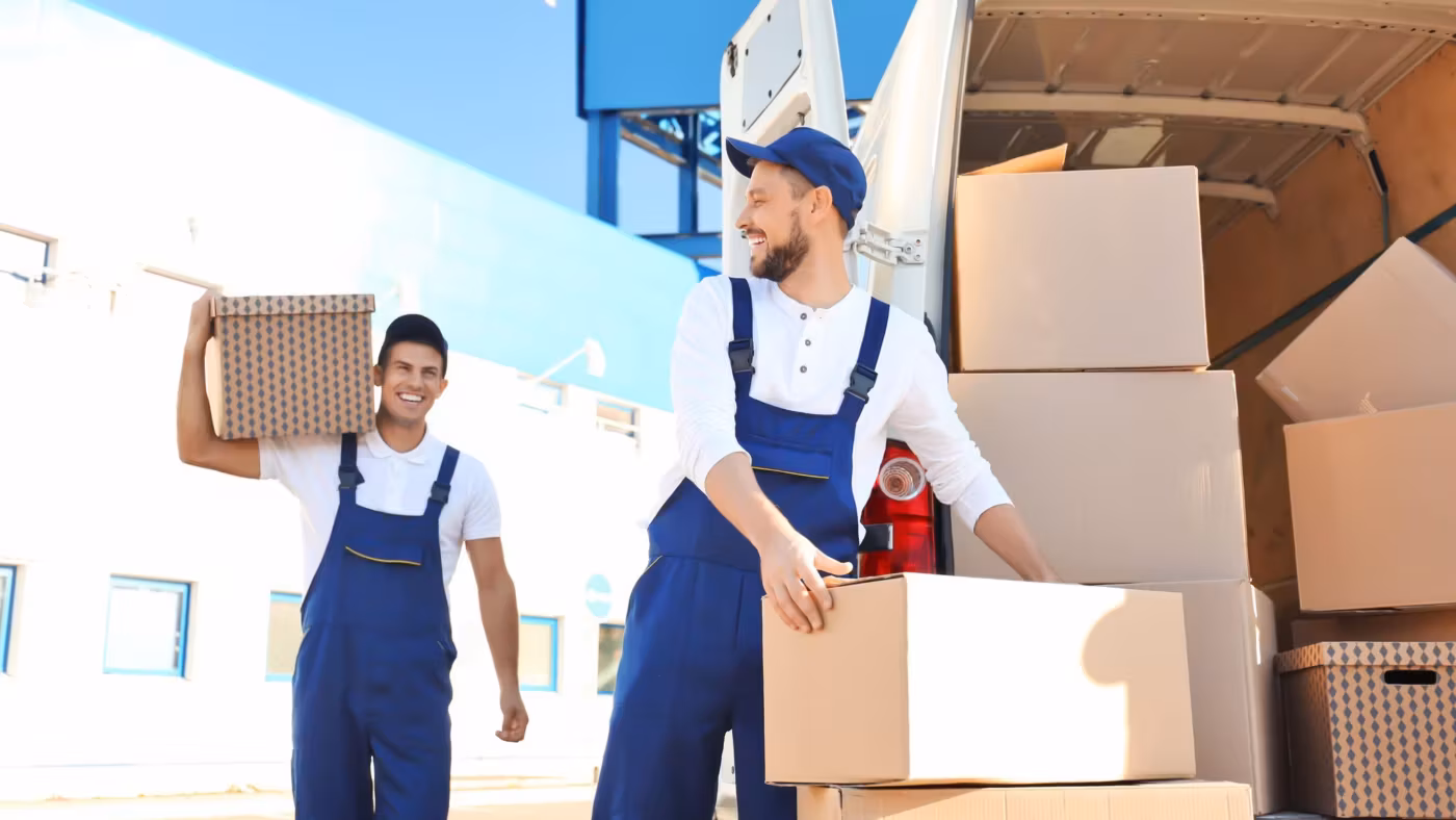 Two movers carrying cartons across open ground in bright daylight