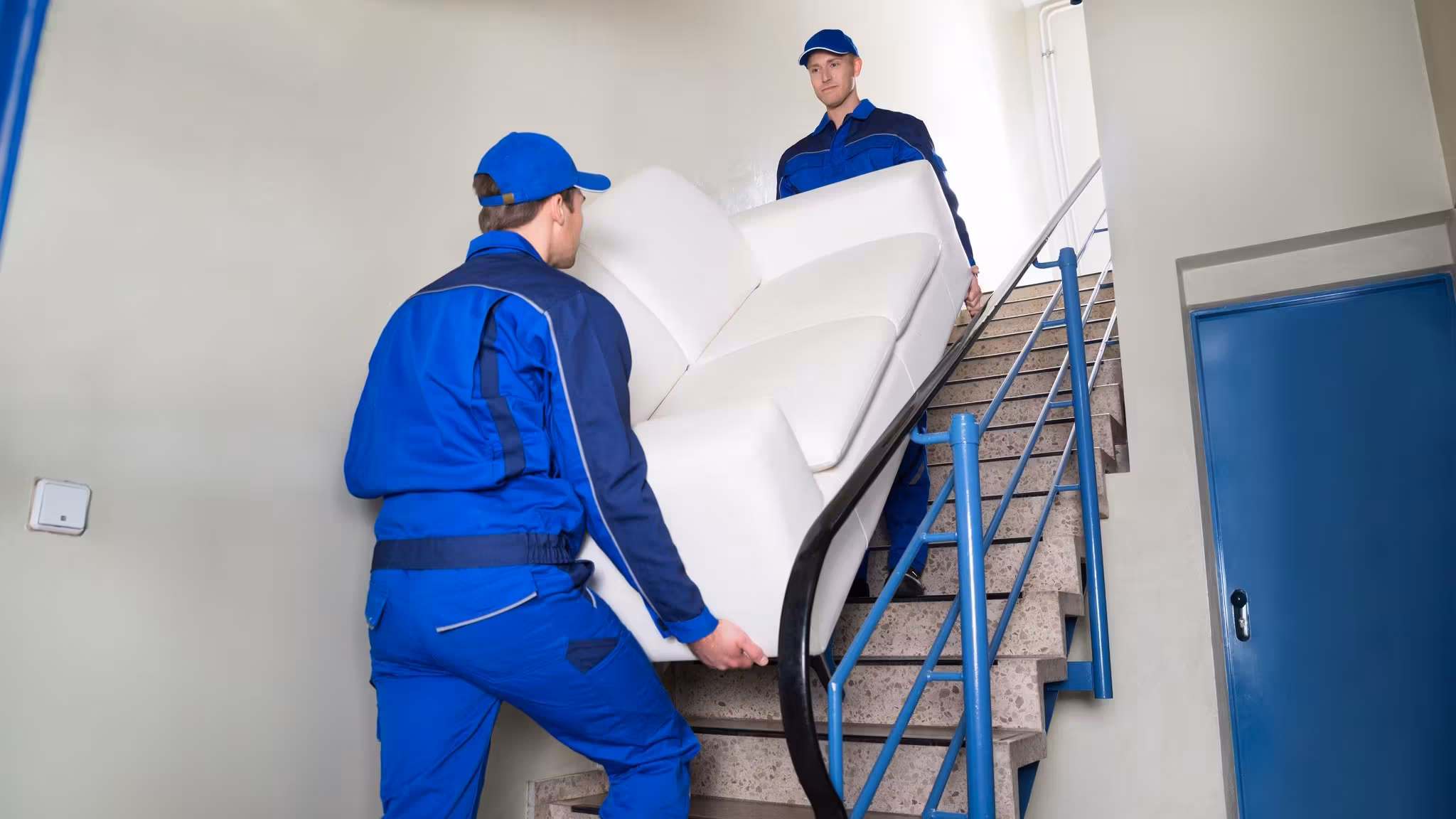 Two movers carrying a wrapped mattress up a staircase