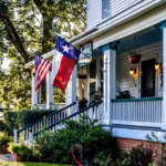 The porch of a white clapboard Texas house with the state and national flags flying