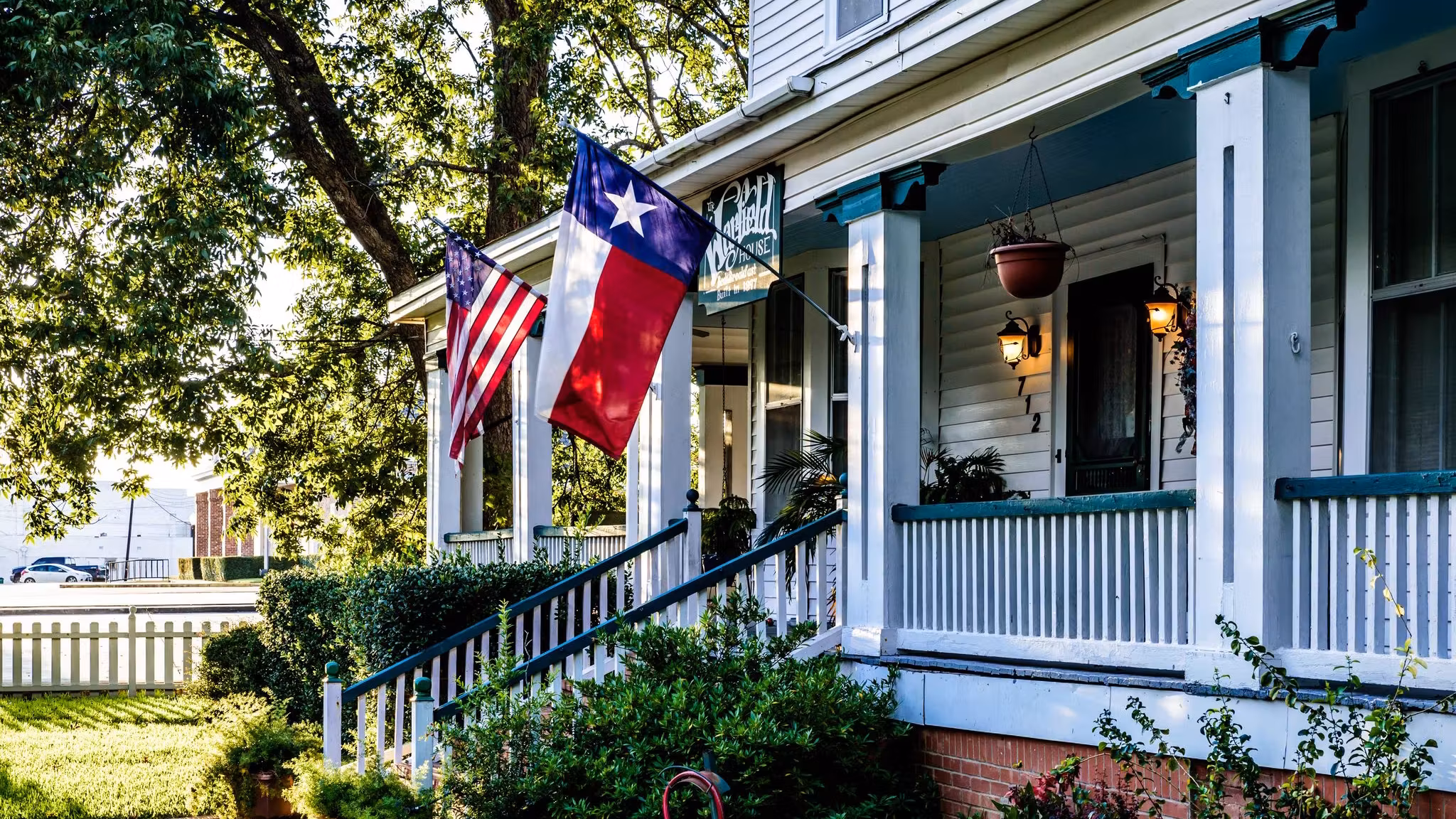 The porch of a white clapboard Texas house with the state and national flags flying