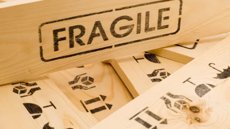 FRAGILE stencilled on pale timber beside printed handling symbols, on the side of a crate