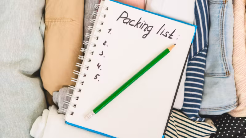 An open notebook headed “Packing list” with a pencil across it, resting on folded clothes