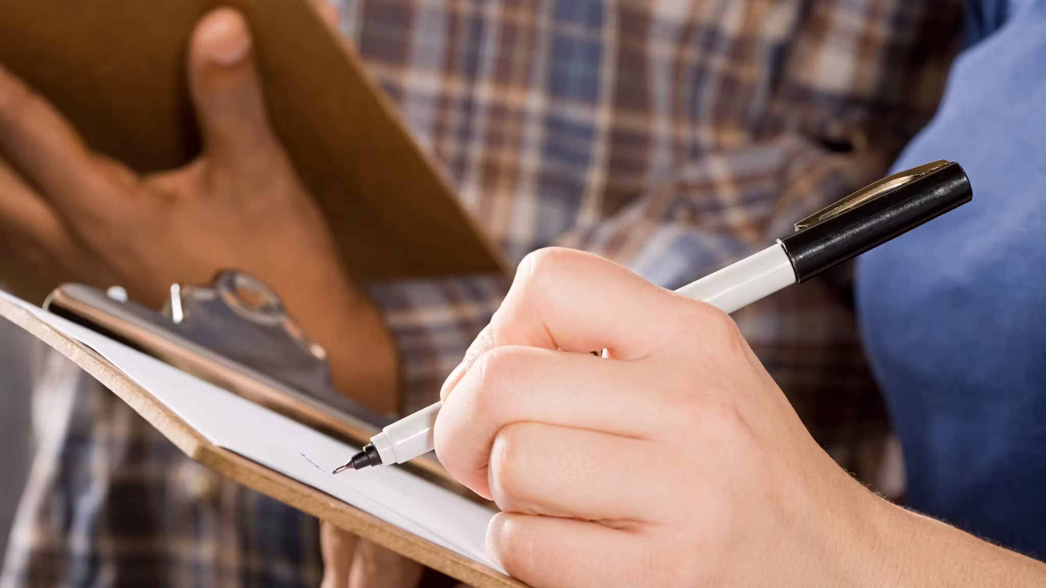 One person signing a form on a clipboard while another holds it steady