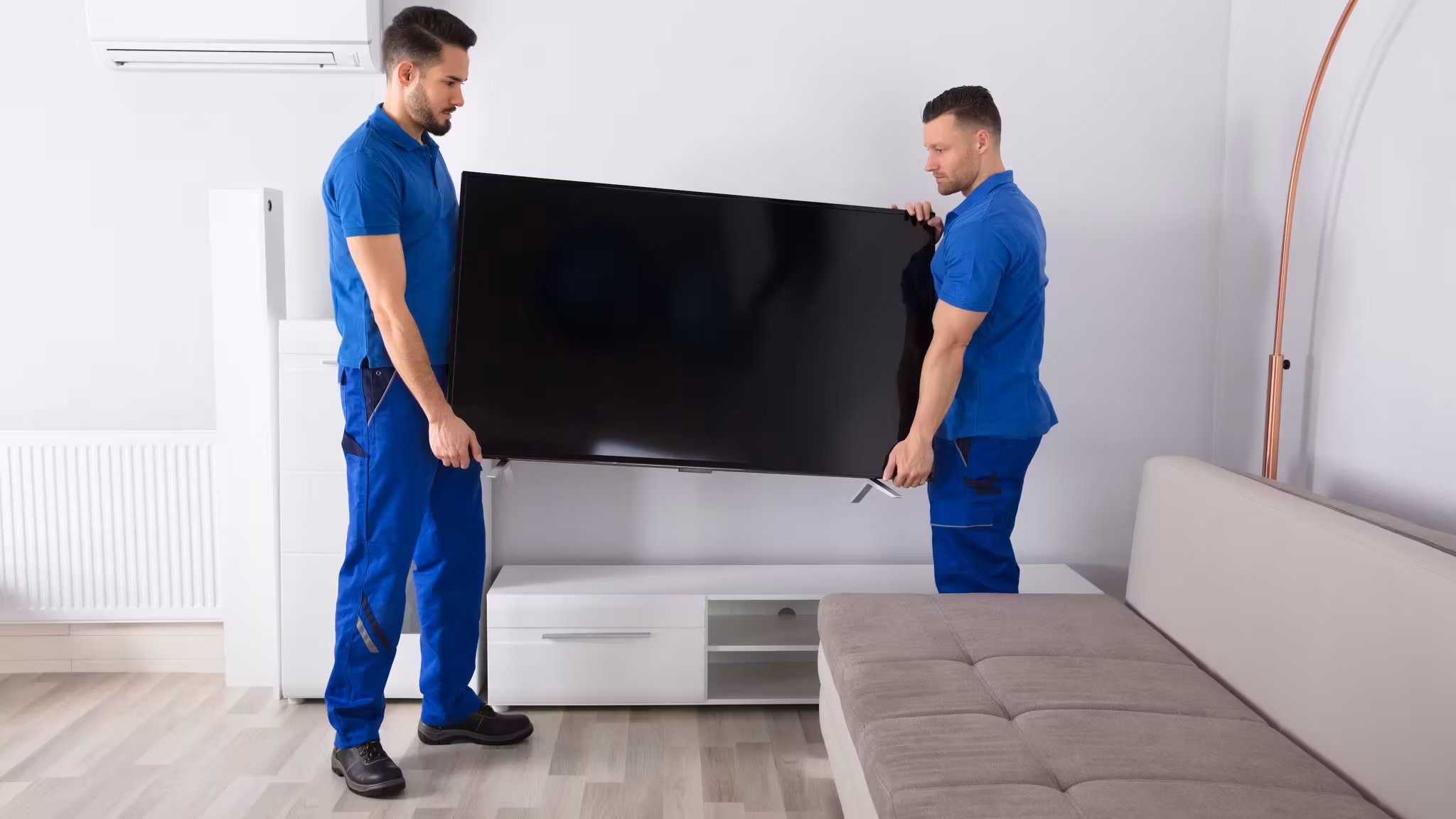 Two movers lifting a large flat-screen television onto a low unit
