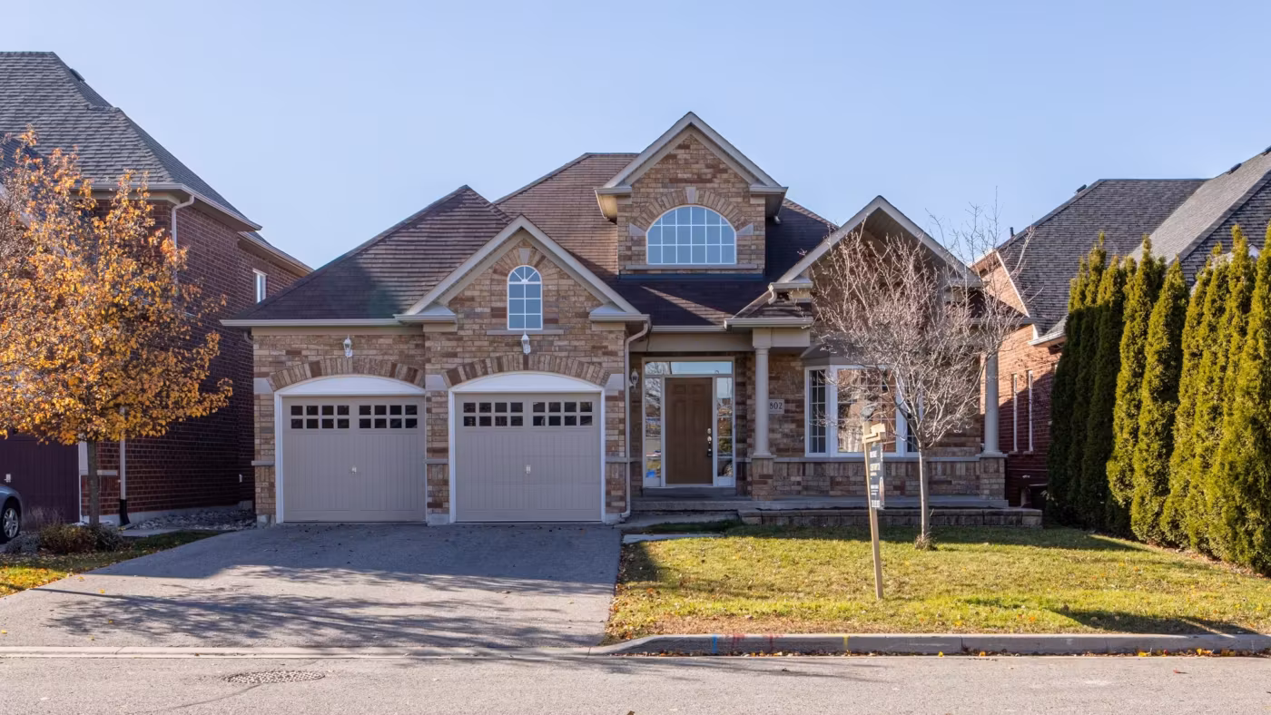 A brick suburban house with a two-car garage and a driveway, seen from the street