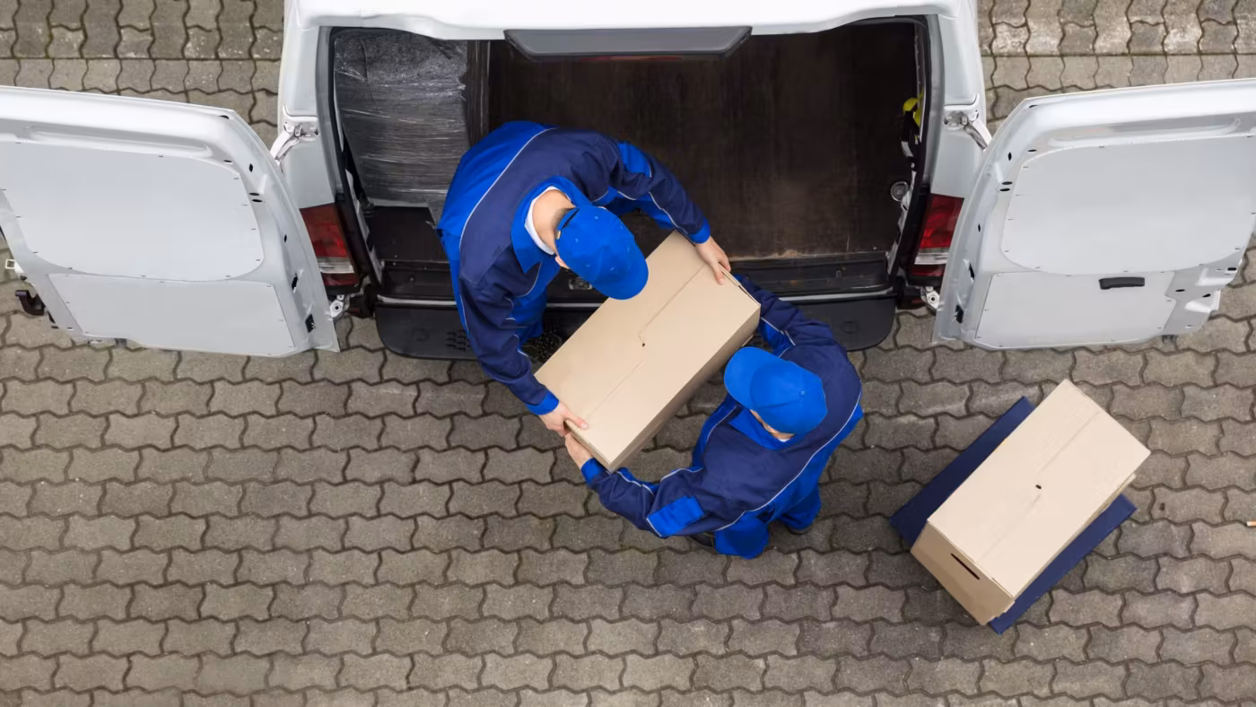 Seen from above, two movers loading a van parked on a paved drive