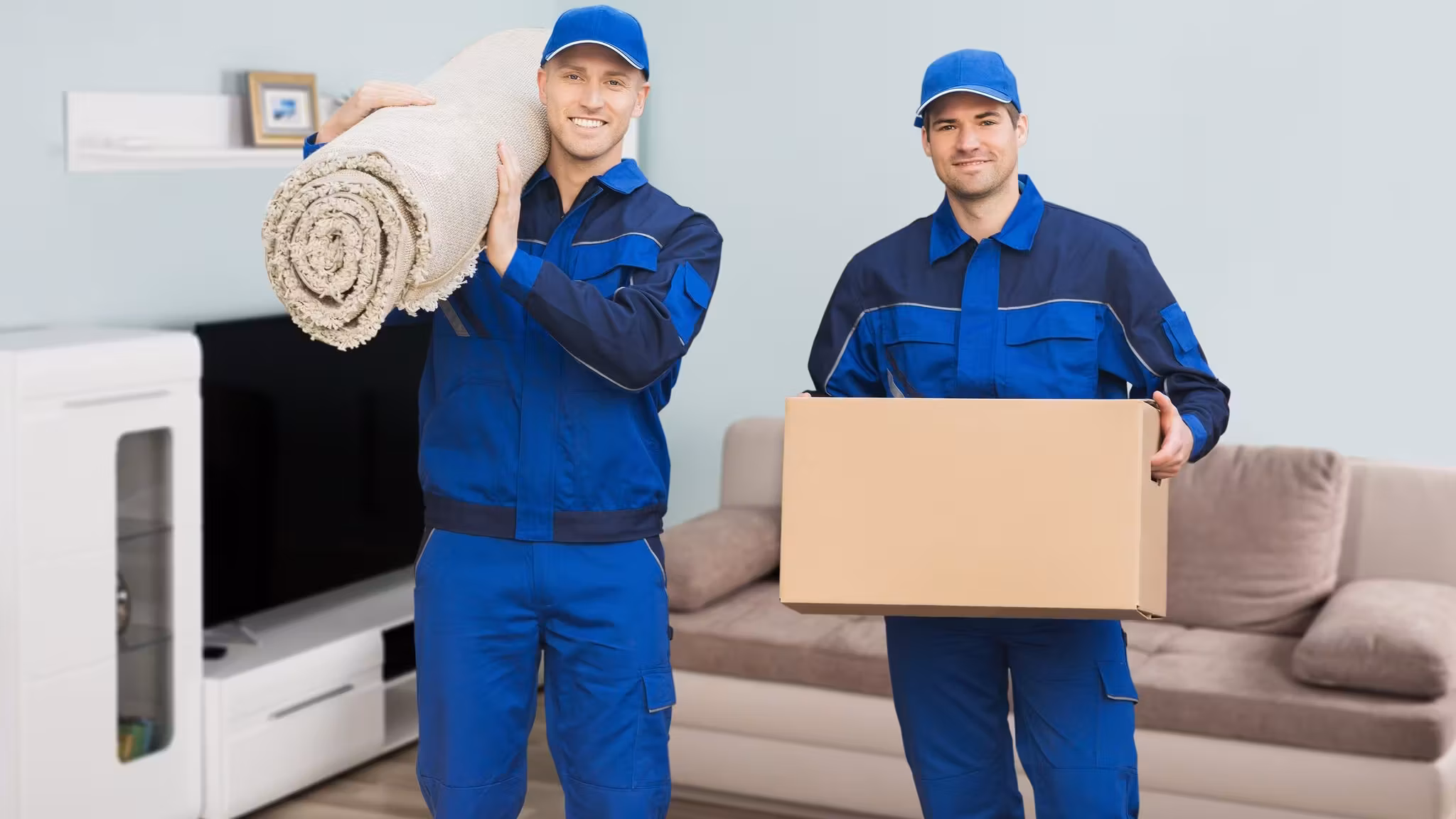 A mover with a rolled rug on his shoulder beside a second carrying a flat screen