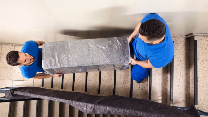 Two movers easing a wrapped item down a staircase