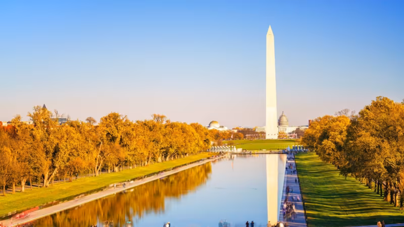 The Washington Monument reflected in the Reflecting Pool with autumn trees along both banks