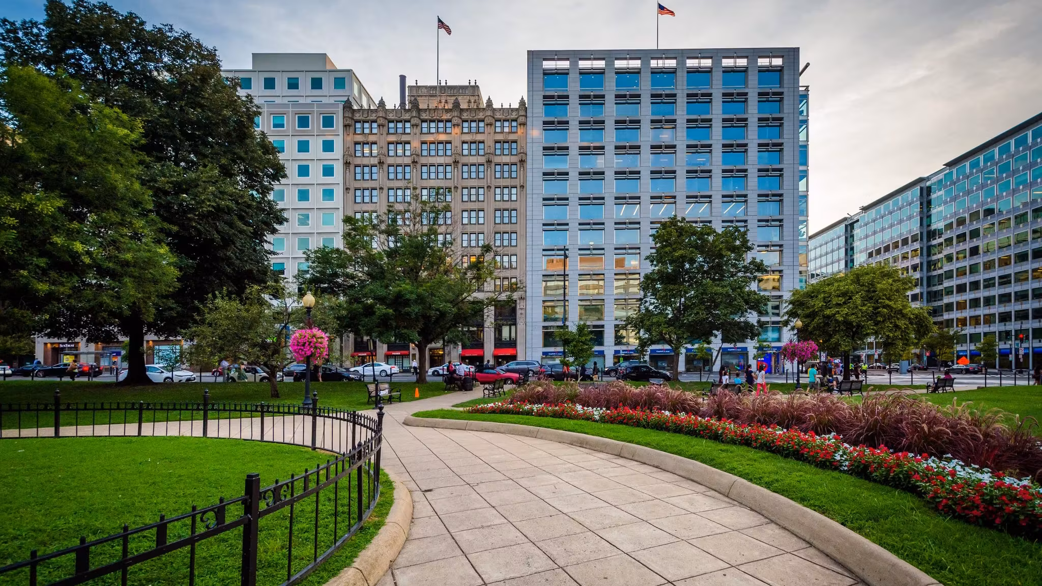A curving path and flower beds in a Washington DC park with office buildings behind