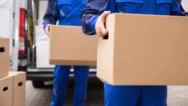 A mover carrying a large carton against his chest, close in