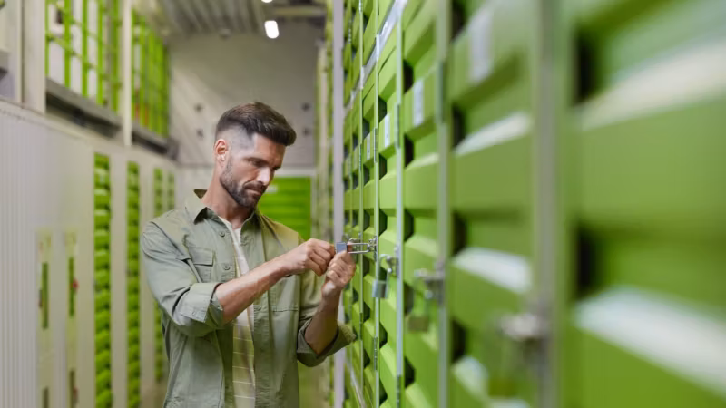 A man at the door of a green storage unit, working the latch