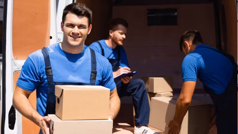 Two movers among cartons, one reading from a tablet