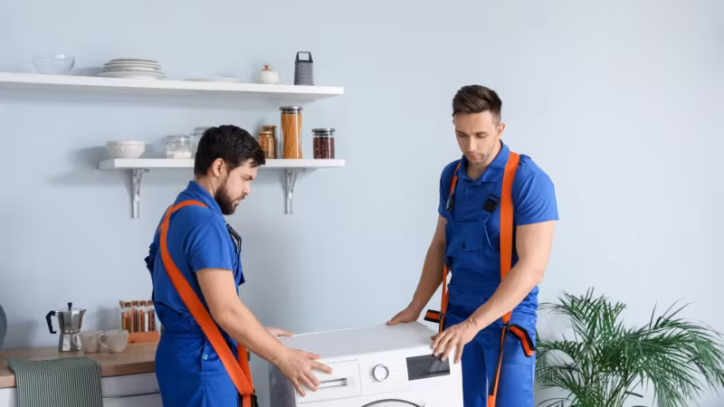 Two movers easing an appliance into place in a utility room