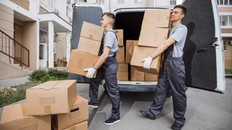 Three movers loading a van from the curb, the load stacked to the roof