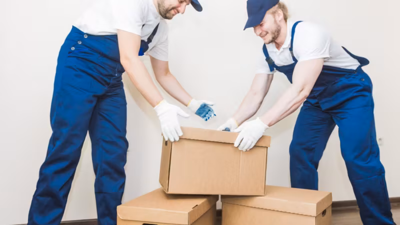 Two movers in gloves closing and taping a carton between them